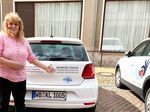 Eine Frau steht an einem Auto und zeigt auf einen darauf befindlichen Aufkleber