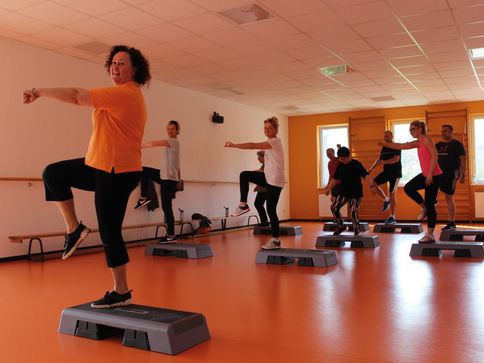 Eine Gruppe Männer und Frauen schauen nach vorne und machen Step-Aerobic