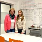 Zwei Frauen stehen an der Schulbank in einem Klassenzimmer vor einer voll beschriebenen Tafel