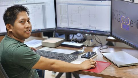 Ein unger Mann sitzt an einem PC vor 3 Bildschirmen