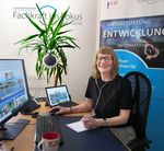 Eine Frau sitzt am Schreibtisch und notiert etwas auf einem Papier