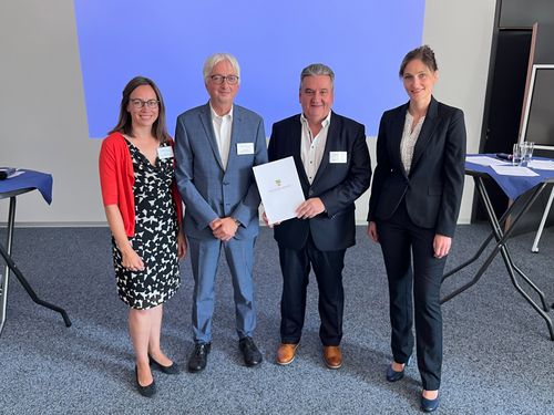 Eine Gruppe von Personen in Businesskleidung steht zusammen, ein Mann hält eine Urkunde des Landes Sachsen-Anhalt in den Händen