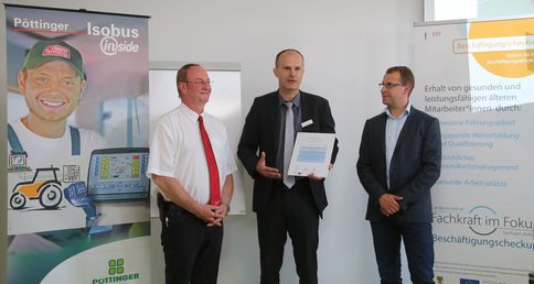 Drei Männer bei Urkundenübergabe