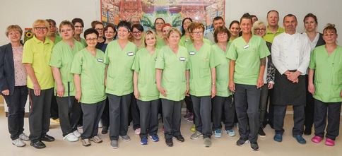 Die Mitarbeiterinnen und Mitarbeiter stehen zusammen und blicken nach vorne in die Kamera