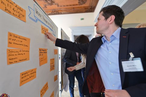 Ein Mann im Anzug heftet beschriebene Karten an eine Pinnwand