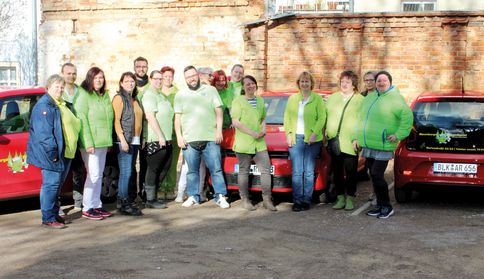 Eine Gruppe von Menschen stehen vor 3 Autos